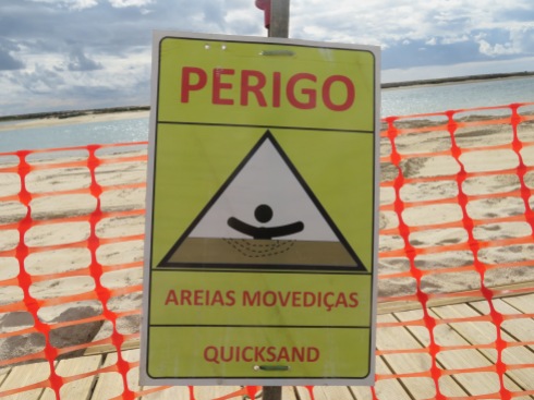 A sign on the beach, completely dug up in places and truck loads of sand piled high in others.